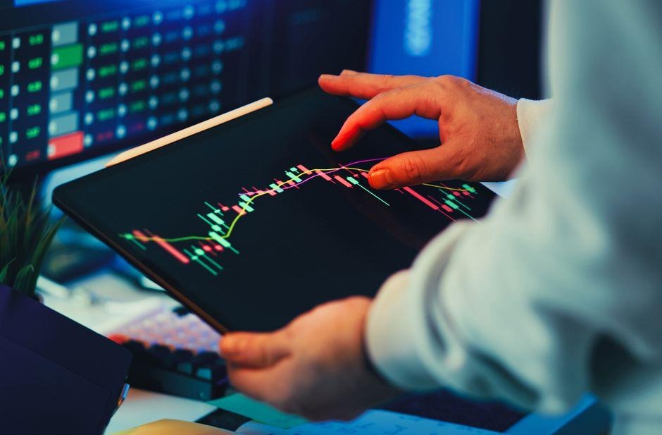 A close-up of a person using a tablet to analyze stock market trends and charts indoors.