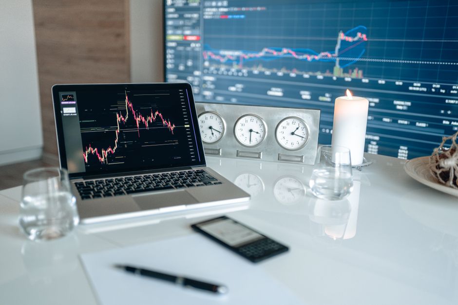 A modern workspace featuring financial charts and multiple clocks on a white table, ideal for trading to illustrate prop firm trading without time limits